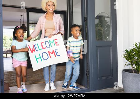 Eine junge birassische Mutter steht mit einem Willkommensschild, flankiert von einem aufgeregten afroamerikanischen Mädchen Stockfoto