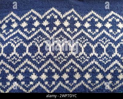 Ein Bruchstück eines Ornaments auf einem gestrickten Polyester- oder Wollpullover. Wintermotive. Rhombusse, gebrochene Linien, Wellen und Kreise. Blaue Gewinde für die Hand Stockfoto