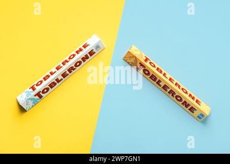 Nahaufnahme von Toblerone Schokolade schweizer Milchschokolade und schweizer weiße Schokolade mit Honig und Mandelnougat auf blauem und gelbem Hintergrund. Il Stockfoto