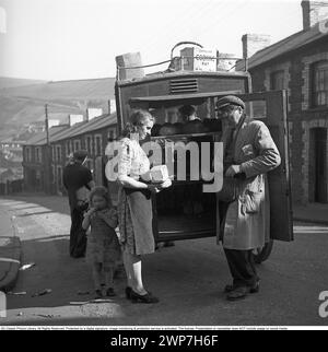 Brot kaufen 1945. Das Dorf Tylorstown im Rhondda-Tal in Wales. Tylorstown wurde Mitte des 19. Jahrhunderts durch den Kohlebergbau an diesem Standort gegründet. Eine einheimische Frau hält das Brot, das sie gekauft hat, und wartet auf Wechselgeld von einem Mann, der Brot und Essen im Dorf aus seiner Pferdekutsche verkauft. Ihre Tochter steht neben ihr in sichtbar abgetragenen Kleidern und nicht so sauberem Gesicht. Oben auf dem Schlitten befinden sich Kartons mit der Aufschrift Compound Cooking FAT. Foto des schwedischen Fotografen KG Kristoffersson, der 1945 in Großbritannien war. ref. S102-3 Stockfoto