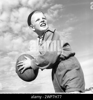 Rugby 1940. Ein junger Rugbyspieler hält den Rugbyball in der Hand und sucht jemanden, auf den er werfen kann. Der Rugbyball hat eine ovale Form, vier Panels und ein Gewicht von etwa 400 Gramm. 1942. Kristoffersson Ref. A56-4 Stockfoto