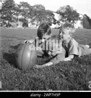 Rugby 1940. Drei junge Rugbyspieler liegen im Gras auf dem Rugbyfeld, einer hält den Rugbyball. Der Rugbyball hat eine ovale Form, vier Panels und ein Gewicht von etwa 400 Gramm. 1942. Kristoffersson Ref. A56-4 Stockfoto