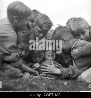 Rugby 1940. Eine Gruppe junger Rugbyspieler, alle auf einem lächelnden Jungen, der sich am Rugbyball festhält. Der Rugbyball hat eine ovale Form, vier Panels und ein Gewicht von etwa 400 Gramm. 1942. Kristoffersson Ref. A56-5 Stockfoto