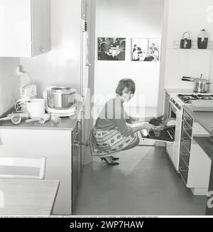 In der Küche in den 1960ern Eine junge Frau in der Küche, die das fertig gebackene Brot aus dem Ofen holt. Der Essensprokossor im typischen 1960er-Look ist auf der Küchenzeile zu sehen. Schweden 1963. ref. BV79-9 Stockfoto