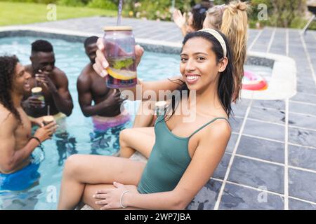 Eine junge Frau in grünem Badeanzug hält einen Drink und lächelt bei einer Poolparty Stockfoto