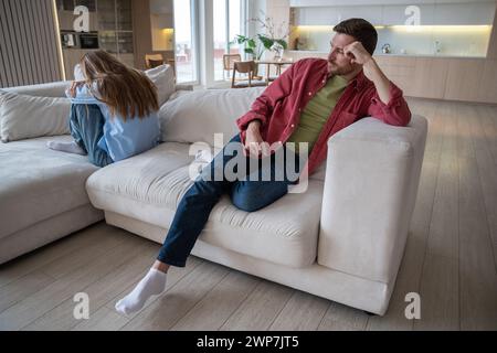 Junges verheiratetes Paar, das an den anderen Enden des Sofas sitzt, mit Groll auf den Gesichtern nach ernstem Streit Stockfoto