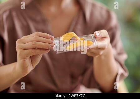 Hände einer Frau, die aufhellende und straffende Augenflecken aus der Packung nimmt Stockfoto