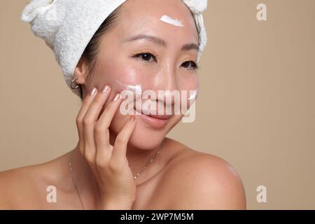 Porträt einer lächelnden Frau, die nach dem Bad eine pflegende Gesichtsmaske aufträgt Stockfoto