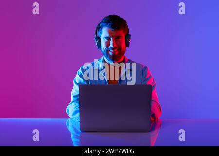 Freiberuflicher Mann mit Headset, der im Neon-Studio am Laptop arbeitet Stockfoto