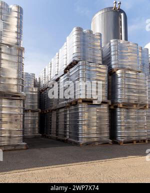 Große Menge an Aluminium-Bierfässern, die mit Euro-Paletten übereinander gestapelt und mit Vinylfolie umwickelt sind. Das Bier, das zum Versand bereit ist, ist eine Flasche Stockfoto