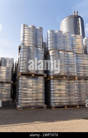 Große Menge an Aluminium-Bierfässern, die mit Euro-Paletten übereinander gestapelt und mit Vinylfolie umwickelt sind. Das Bier, das zum Versand bereit ist, ist eine Flasche Stockfoto