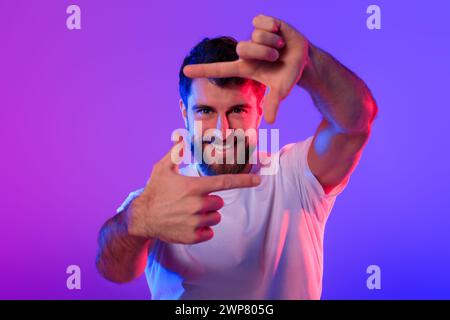 Fröhlicher kaukasier, der mit Fingern Bilderrahmen macht, Neonhintergrund Stockfoto