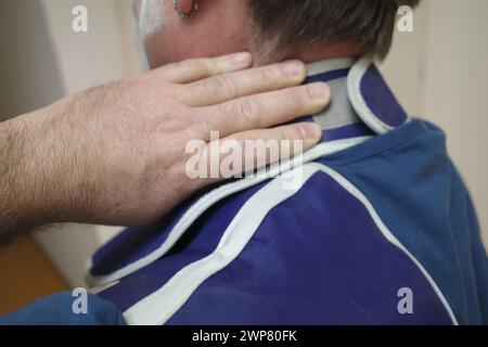 Ein Mann in blauem Hemd, der Nackenschmerzen von der Arbeit hat Stockfoto
