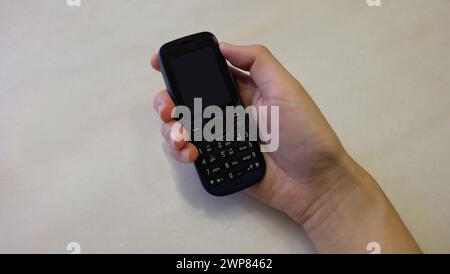 Hand hält ein schwarzes, veraltetes Handy mit leerem Bildschirm. Stockfoto