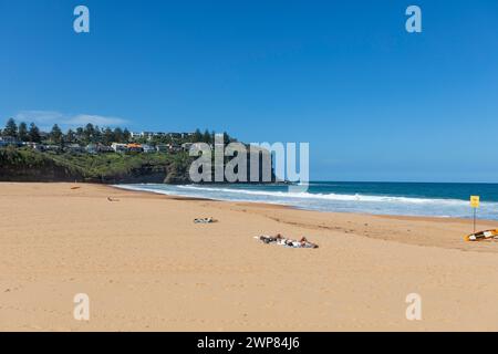 Ein paar Sonnenbaden am Bilgola Beach an Sydney Northern Beaches, NSW, Australien mit klarem blauen Himmel und sanften Wellen Stockfoto