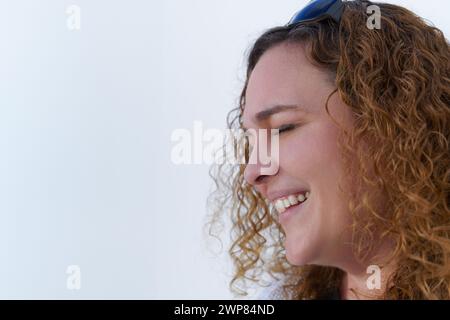 Attraktive Frau mit langen lockigen Haaren im Profil gesehen, lächelnd mit geschlossenen Augen auf weißem Hintergrund und Kopierraum Stockfoto