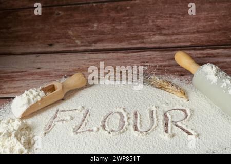 Gesiebtes Mehl auf einem Holztisch, auf dem das Wort Mehl steht, neben einem Weizenohr und einer Nudelnadel, Holzboden und Kopierraum Stockfoto