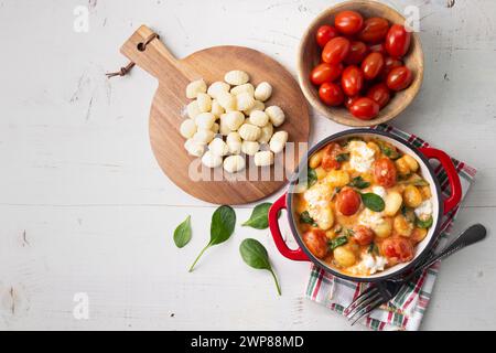 Gnocchi-Auflauf in cremiger Tomatensauce mit Babyspinat und geschmolzenem Mozzarella auf weißem Holztisch. Draufsicht Stockfoto