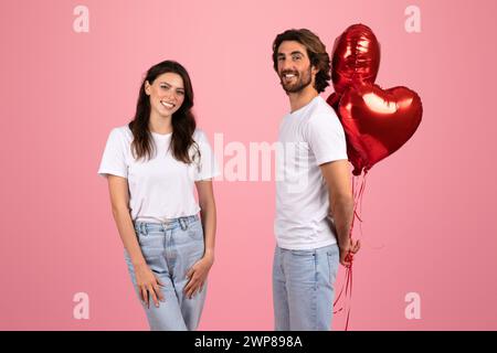 Lächelnde Frau und Mann in weißen T-Shirts, mit einem Haufen roter Herzballons Stockfoto
