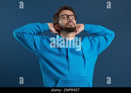 Zufriedener junger Mann in Brille, der mit Händen hinter dem Kopf zurückliegend Stockfoto