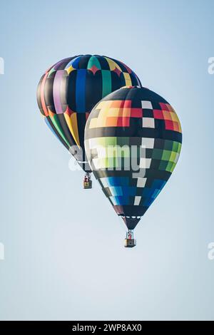 Zwei lebhafte Heißluftballons fliegen zusammen am klaren Himmel in Iowa Stockfoto