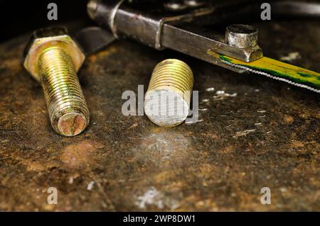 Ein abgesägter Bolzen und eine Metallsäge liegen auf einem rostigen Metall Stockfoto