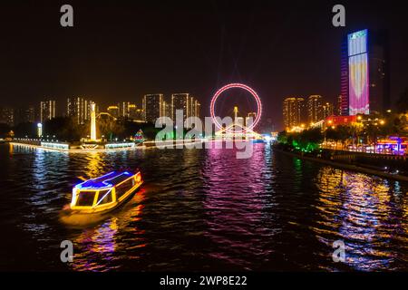 Nachtansicht über das beleuchtete Touristenboot und das Riesenrad in Tianjin, China Stockfoto