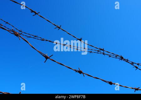 Stacheldraht, Draht, schmaler Streifen aus Metallband, mit scharfen Spitzen darauf, die als Barrieren verwendet werden. Rostiger Stacheldraht gegen den blauen Himmel. Die Stockfoto