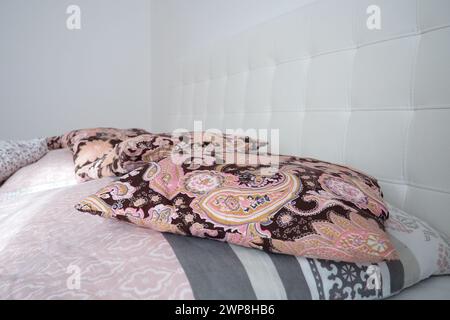 Pinke dekorative Kissen auf der Bettwäsche. Doppel-Hochzeitsbett mit Kissen und dicker Federdecke. Schlafzimmerdesign. Weiches weißes Kopfteil. Innenraum mit Stockfoto