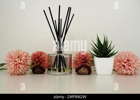 Zusammensetzung rosa künstlicher Blüten, Weihrauchstäbchen in einer Glasvase mit ätherischem Öl. Stillleben auf einem weißen Tisch. Aloe-Blume in einem weißen Topf. Ro Stockfoto