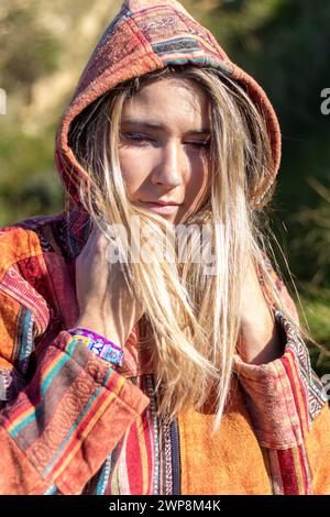 Eine Frau mit langen blonden Haaren trägt eine bunte Jacke mit Kapuze. Sie blickt mit einem nachdenklichen Ausdruck in die Kamera Stockfoto