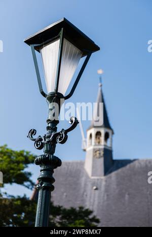 Nahaufnahme einer klassischen Straßenlaterne im Dorf Oudenhoorn in den Niederlanden. Im Hintergrund steht die reformierte evangelische Kirche. Stockfoto