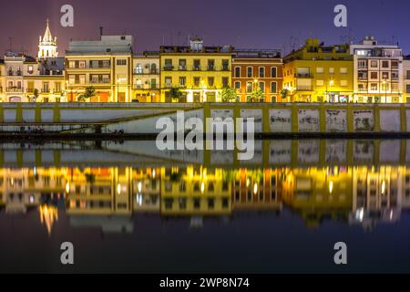 Gebäude und Lichter der Calle Betis spiegeln sich in der Abenddämmerung an der Oberfläche des Flusses. Stockfoto