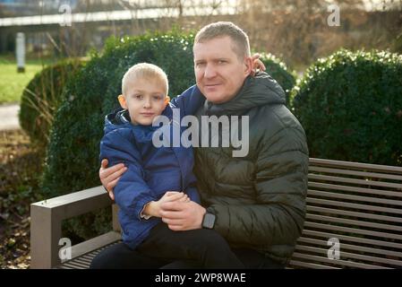 Herbstliche Familienzusammenhänge: Vater, 40 Jahre alt, und Sohn - wunderschöner 8-jähriger Junge, im Park sitzend. Stockfoto