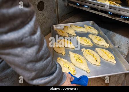 Alte Mannhände halten einen Aluminiumteller voll mit Weißkäse gefülltem Gebäck und stellen ihn in den alten Ofen Stockfoto