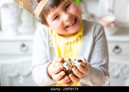 3. März 2024: Eierjagd, kleiner Junge, der mehrere Wachteleier für Ostern hält. Kind mit selbstgebauten Hasenohren auf dem Kopf *** Eiersuche, kleiner Junge hält mehrere Wachteleier zu Ostern in der Hand. Kind mit selbstgebastelten Hasenohren auf dem Kopf Stockfoto