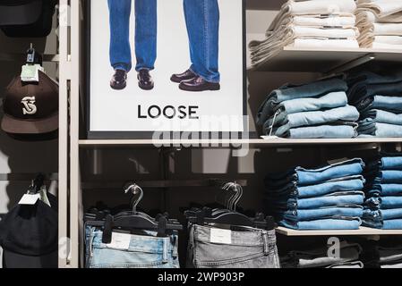 Lose Jeans auf Regalen und Poster, auf denen die losen Hosen im H&M Store am 3. März 2024 in Bangkok, Thailand, erklärt werden. Stockfoto