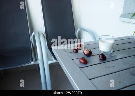 Kastanienfrüchte auf dem Tisch. Tisch und Stühle auf dem Balkon oder der Terrasse. Saisonende im Hotel. Der Tisch ist silberfarben gestrichen. Stockfoto