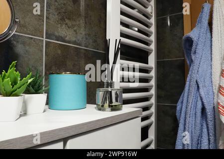 Elemente zur Badeinrichtung. Ein blaues Glas mit Creme und grünen Pflanzen in kleinen weißen Töpfen befindet sich auf einem Regal im Schrank. Schwarze Wandfliesen. Badezimmer innen Stockfoto