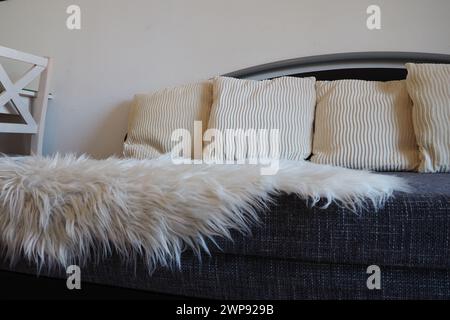 Graues Sofa mit boucle-Polsterstoff und weißen dekorativen geriffelten Kissen. Weißer Teppich oder Bettüberwurf aus Kunstfell mit langem Stapel. Wohnzimmer Stockfoto