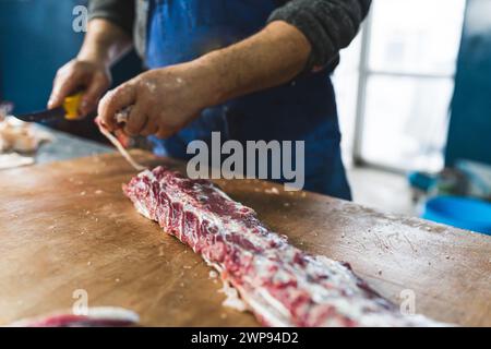 Ein Metzger, der Schweinerippen auf dem Holztisch schneidet, Nahaufnahme Schlachthof. Hochwertige Fotos Stockfoto