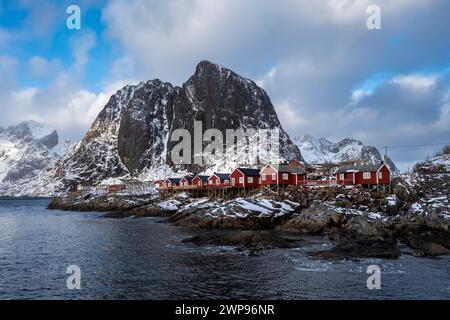Blick auf die Insel Hamnøya mit dem berühmten roten rorbuer und den Lilandstinden in der reinen Bucht im Winter. Lofoten-Inseln, Norwegen. Stockfoto