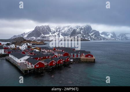 Blick auf die Insel Hamnøya mit dem berühmten roten rorbuer und den Lilandstinden in der reinen Bucht im Winter. Lofoten-Inseln, Norwegen. Stockfoto