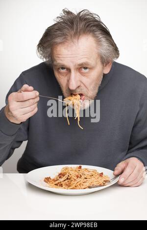 Ein älterer Mann isst Spaghetti mit Hackfleisch, Tomaten und Käse Stockfoto