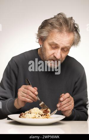 Ein älterer Mann isst Spaghetti mit Hackfleisch, Tomaten und Käse Stockfoto