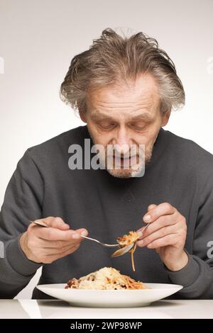 Ein älterer Mann isst Spaghetti mit Hackfleisch, Tomaten und Käse Stockfoto