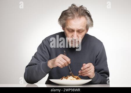 Ein älterer Mann isst Spaghetti mit Hackfleisch, Tomaten und Käse Stockfoto