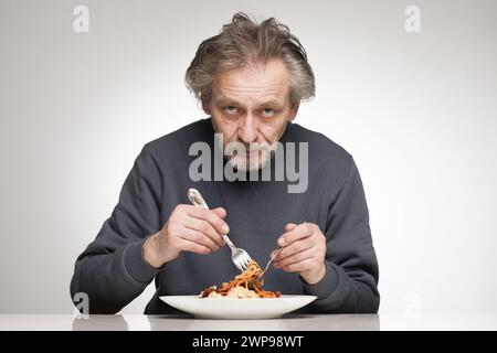 Ein älterer Mann isst Spaghetti mit Hackfleisch, Tomaten und Käse Stockfoto