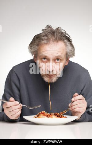 Ein älterer Mann isst Spaghetti mit Hackfleisch, Tomaten und Käse Stockfoto