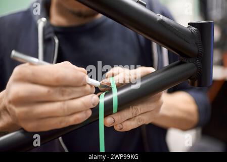 Unerkennbarer Mann, der einen Fahrradrahmen mit einem Skalpell und Abdeckband für eine individuelle Bemalung in seiner Fahrradwerkstatt vorbereitet. Stockfoto